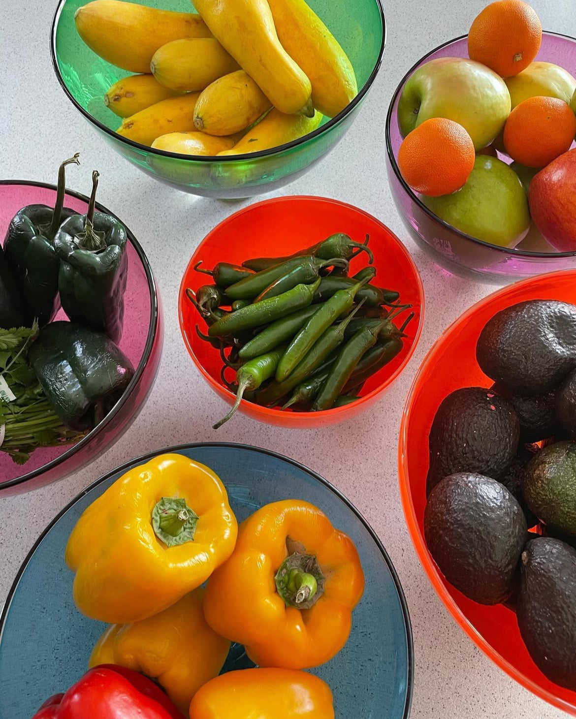 Assorted fruits and vegetables in colorful blown glass bowls on a table.